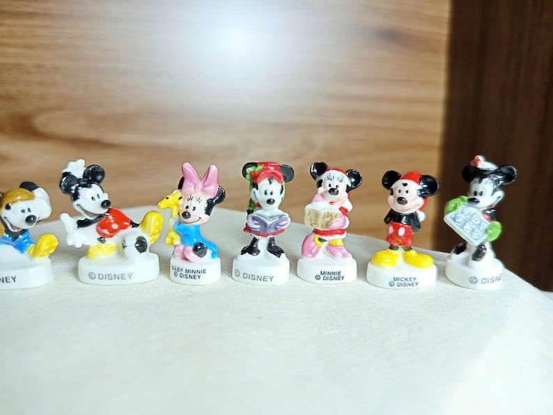 Puede incluir: Colecci&oacute;n de siete figuras de personajes de Disney, incluyendo Mickey Mouse, Minnie Mouse y Donald Duck. Cada figura est&aacute; sobre una base blanca con la palabra "Disney". Las figuras son de colores brillantes y miden unos 5 cm de altura.