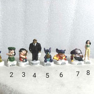 May include: A collection of eight small, colorful Disney character figurines. The figurines include characters like Stitch, Lilo, and Jumba. Each figurine is on a white base with the character's name and "Disney" printed on it.