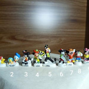May include: A collection of nine small Disney character figurines. The figurines include Donald Duck, Baby Donald, Mickey Mouse, and Goofy. Each figurine is on a white base with the character's name.