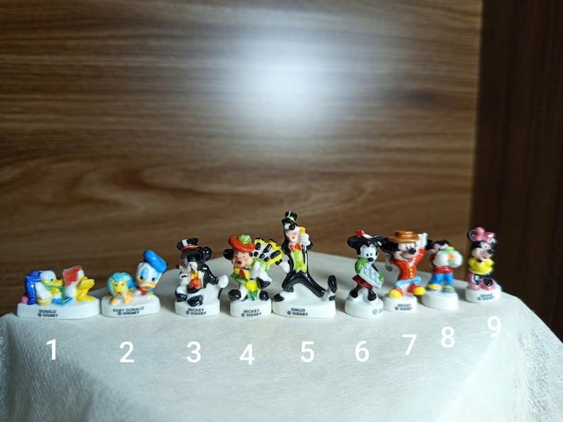 以下が含まれることがあります： 9体の小さなディズニーキャラクターのフィギュアのコレクション。フィギュアには、ドナルドダック、ベビードナルド、ミッキーマウス、グーフィーが含まれます。各フィギュアは、キャラクターの名前が書かれた白いベースにあります。