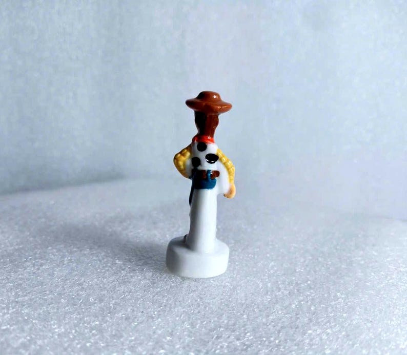 Pu&ograve; includere: Piccola e dettagliata statuina del personaggio Woody del film d'animazione Toy Story. La statuina presenta un cappello da cowboy marrone, una camicia gialla, un fazzoletto rosso e un gilet blu. La figura &egrave; montata su una base bianca.