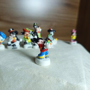 以下が含まれることがあります： 小さくてカラフルなディズニーキャラクターのフィギュアのコレクション。ミッキーマウスは前面にあり、赤いショーツ、黄色のシャツ、青い靴を履いています。他のキャラクターには、ドナルドダック、ミニーマウス、グーフィーが含まれます。フィギュアは白い台座にあります。