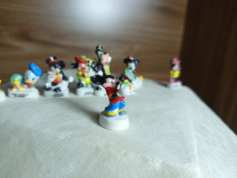 以下が含まれることがあります： 小さくてカラフルなディズニーキャラクターのフィギュアのコレクション。ミッキーマウスは前面にあり、赤いショーツ、黄色のシャツ、青い靴を履いています。他のキャラクターには、ドナルドダック、ミニーマウス、グーフィーが含まれます。フィギュアは白い台座にあります。