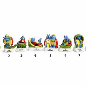 May include: A collection of eight small, colorful ceramic figurines. Each figurine features a blue cat-like character in various poses, with French text at the base. The figurines are numbered 1 through 8.