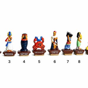 May include: A collection of eleven small, colorful ceramic figurines, each depicting a zodiac sign. The figurines are on brown bases with the sign's name. The figures include a bull, a person with a bird head, and a lion.