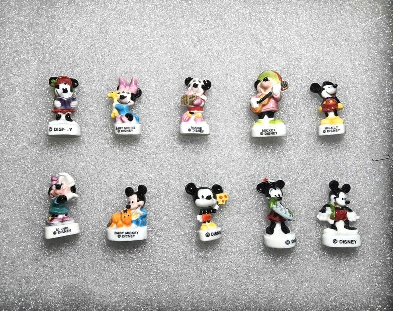 May include: A set of ten miniature Disney character figurines. The figures depict Mickey Mouse, Minnie Mouse, and other characters in different outfits. Each figurine stands on a white base with the Disney name.