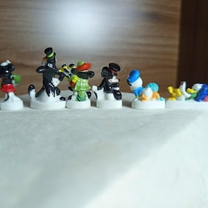 以下が含まれることがあります： 漫画のキャラクターをフィーチャーした、小さくてカラフルなフィギュアのコレクション。 フィギュアは白い台座にあり、さまざまなポーズや衣装のキャラクターがいます。 フィギュアはセラミックまたは同様の素材で作られています。