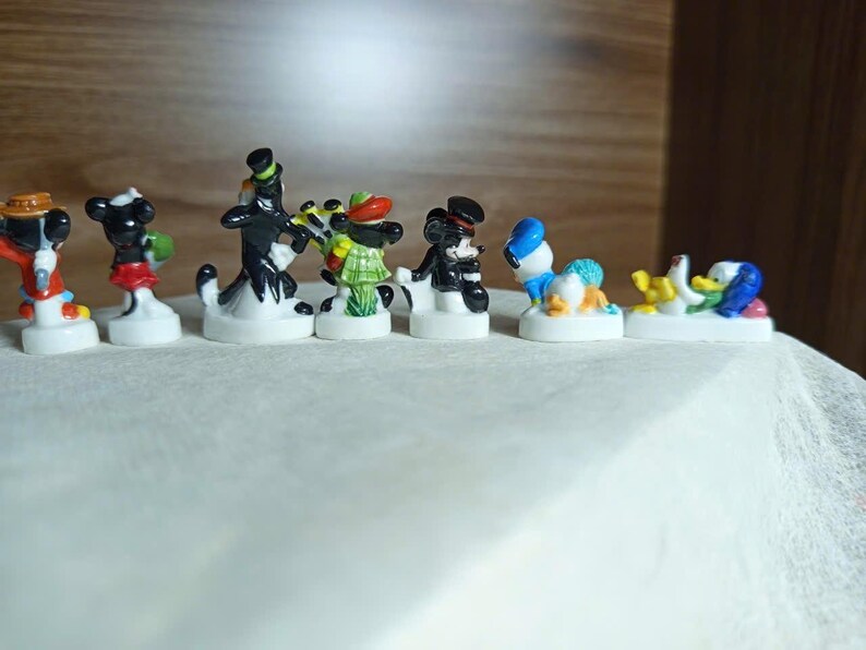 以下が含まれることがあります： 漫画のキャラクターをフィーチャーした、小さくてカラフルなフィギュアのコレクション。 フィギュアは白い台座にあり、さまざまなポーズや衣装のキャラクターがいます。 フィギュアはセラミックまたは同様の素材で作られています。