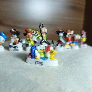 以下が含まれることがあります： ミッキーマウス、ドナルドダックなど、ディズニーのキャラクターの小さなカラフルなフィギュアのコレクション。各フィギュアは、キャラクターの名前が書かれた小さな白いベースに取り付けられています。フィギュアは明るい色で、細部までこだわっています。