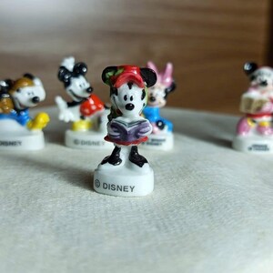 Puede incluir: Una colecci&oacute;n de peque&ntilde;as figuras de personajes de Disney. Las figuras incluyen a Mickey Mouse, Minnie Mouse y otros personajes. Cada figura est&aacute; sobre una base blanca con la palabra "DISNEY" impresa. Las figuras est&aacute;n pintadas con colores brillantes.