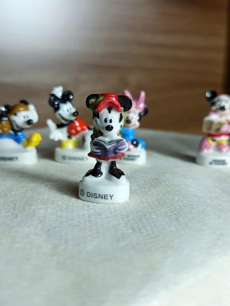 Puede incluir: Una colecci&oacute;n de peque&ntilde;as figuras de personajes de Disney. Las figuras incluyen a Mickey Mouse, Minnie Mouse y otros personajes. Cada figura est&aacute; sobre una base blanca con la palabra "DISNEY" impresa. Las figuras est&aacute;n pintadas con colores brillantes.
