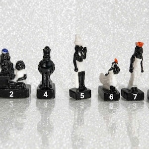 Puede incluir: Una colección de figuras en miniatura en blanco y negro, cada una sobre una pequeña base negra. Las figuras representan varias figuras, algunas con detalles en azul o naranja. Las figuras están numeradas del 1 al 7.