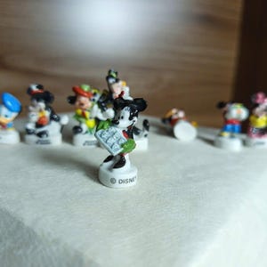 以下が含まれることがあります： ミッキーマウス、ドナルドダックなど、小さなディズニーキャラクターのフィギュアのコレクション。フィギュアは明るい色で、白い台座に立っています。ディズニーのロゴが1つに表示されています。