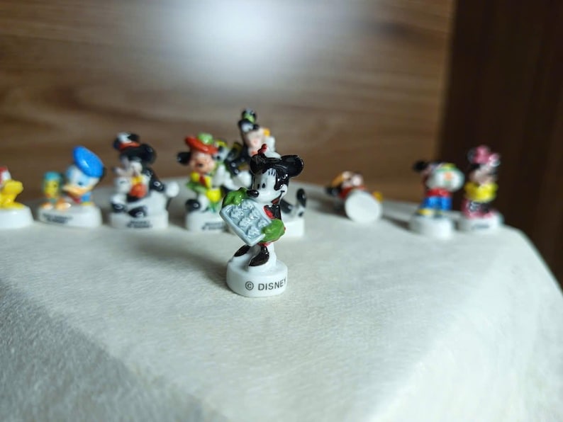 以下が含まれることがあります： ミッキーマウス、ドナルドダックなど、小さなディズニーキャラクターのフィギュアのコレクション。フィギュアは明るい色で、白い台座に立っています。ディズニーのロゴが1つに表示されています。