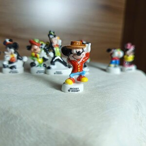 以下が含まれることがあります： 小さなカラフルなディズニーキャラクターのフィギュアのコレクション。ミッキーマウスは赤いジャケットと茶色の帽子をかぶっています。他のキャラクターには、ドナルドダック、ミニーマウス、グーフィーが含まれます。各フィギュアは、「ミッキーディズニー」のロゴが入った白いベースにあります。