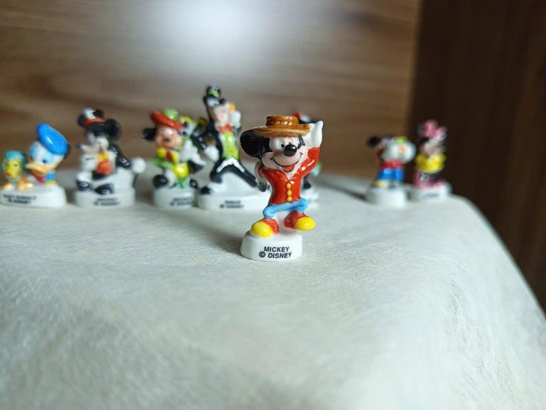 以下が含まれることがあります： 小さなカラフルなディズニーキャラクターのフィギュアのコレクション。ミッキーマウスは赤いジャケットと茶色の帽子をかぶっています。他のキャラクターには、ドナルドダック、ミニーマウス、グーフィーが含まれます。各フィギュアは、「ミッキーディズニー」のロゴが入った白いベースにあります。