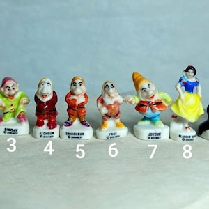 May include: A collection of ten small ceramic figurines featuring characters from the Snow White fairytale. The figurines include the seven dwarfs, Snow White, the Evil Queen, and a numbered base.