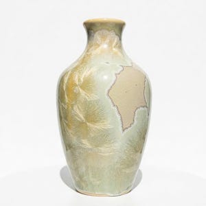 May include: A ceramic vase with a unique crystalline glaze. The vase features a light green and beige color palette with a textured surface. The vase has a rounded body and a narrow neck. The overall height is approximately 8 inches.