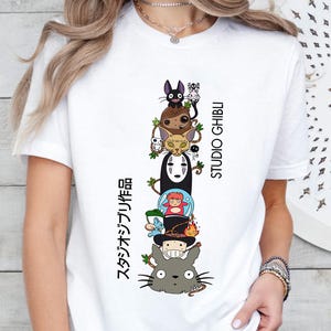 May include: White t-shirt featuring a stacked graphic of Studio Ghibli characters, including Totoro, No-Face, and others. The text "STUDIO GHIBLI" and Japanese text are printed vertically on the right and left sides of the graphic.