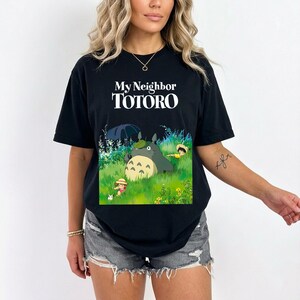 May include: Black t-shirt featuring the text "My Neighbor TOTORO" in white. The graphic depicts Totoro and other characters in a grassy field. The shirt is a short-sleeved, crew neck style.
