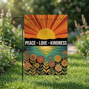 Puede incluir: Una bandera de jardín con un diseño retro que presenta una puesta de sol, agua y flores. La bandera tiene las palabras "PEACE - LOVE - KINDNESS" en texto blanco. La paleta de colores incluye naranja, amarillo, turquesa y negro.