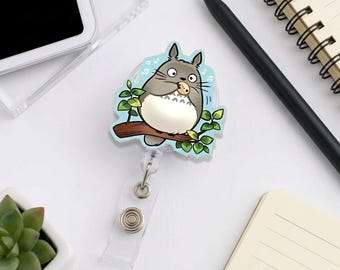 Porta-crachá retrátil em acrílico com clipe para desenho de criatura da floresta em estilo anime e formato de folha.