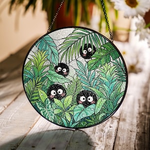 May include: Round stained glass panel featuring a jungle scene with lush green leaves and several black, furry creatures with large eyes. The panel is framed in black and hangs from a chain.