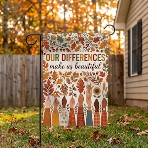 Peut inclure: Un drapeau de jardin rectangulaire portant le texte "OUR DIFFERENCES make us beautiful" en lettres brunes et vertes. Le motif présente diverses feuilles d'automne, des glands et des épis de blé au-dessus de huit bras aux tons de peau variés.