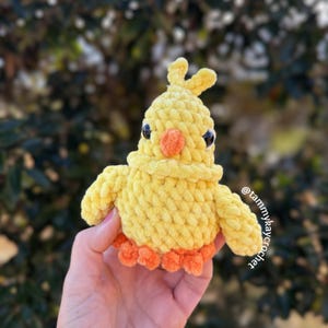 Hand holding no-sew crochet baby chick plush in yellow yarn with orange beak and feet