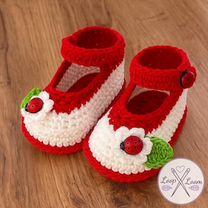 May include: A pair of handmade crochet baby shoes. The shoes are red and white with a Mary Jane style strap. Each shoe features a white flower with a red ladybug center and green leaf accents. A red button secures the strap.
