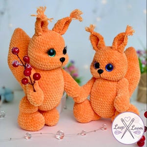 May include: Two plush orange squirrels with large, expressive eyes and fluffy tails. One squirrel holds a sprig of red berries. The squirrels are handmade and have a soft, textured appearance, perfect for a child's toy or nursery decor.