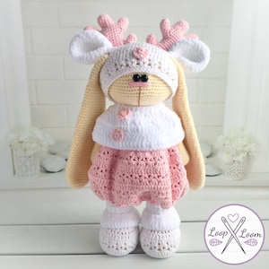 May include: A handmade crochet bunny doll wearing a white hat with pink antlers and a pink dress. The doll has long, floppy ears and is wearing white shoes. The doll is approximately 18 inches tall.