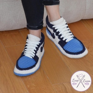May include: Hand-crocheted high-top sneakers in blue, white, and navy. The toe box is blue, with white laces and a navy and white design. The sneakers are designed to resemble popular athletic footwear.