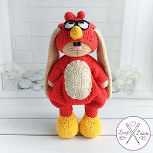 May include: A handmade crochet bunny doll in a red outfit with a matching hat and yellow shoes. The bunny has a beige face, long ears, and a beige oval on its chest. The doll has black glasses and a yellow beak.