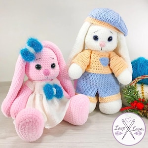 Peut inclure: Deux poupées lapins crochetées à la main. L'une est rose avec une robe blanche et des nœuds bleus. L'autre est blanche avec un chapeau bleu, un haut orange et un short bleu. Les deux ont des yeux noirs et sont assis.
