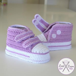 Peut inclure: Une paire de chaussons de bébé au crochet faits à la main, en lavande et blanc. Les chaussures montantes présentent un bout blanc, une bande blanche autour de la semelle et deux fermetures auto-agrippantes. Les chaussures sont en tricot doux et texturé.