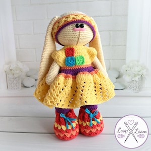 May include: A handmade crochet bunny doll wearing a yellow dress with colorful accents. The doll has long ears, a matching hat, and red and orange shoes with blue bows. The doll is approximately 12 inches tall.