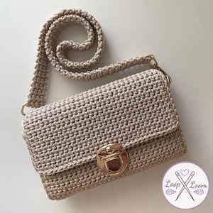 May include: A beige crochet crossbody bag with a gold clasp and strap attachments. The bag has a textured, woven pattern and a long, matching strap. The bag is rectangular with a flap closure.