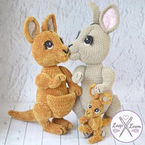 Peut inclure: Trois peluches kangourous au crochet, dans des tons de beige et de marron clair. Les deux grands kangourous s'embrassent, tandis qu'un plus petit se tient devant. Les peluches ont de grands yeux expressifs et sont faites avec une laine douce et texturée.
