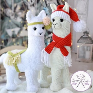 May include: Two white crochet llamas. One llama wears a red and white Santa hat and a red scarf with white fringe. The other llama has a yellow headband with a pink and green pom-pom. Both have black eyes and are standing.