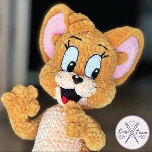 Puede incluir: Juguete de peluche de ratón de dibujos animados tejido a ganchillo, con pelaje marrón, orejas internas rosas y ojos azules. El ratón tiene una expresión sonriente con lengua roja y nariz negra. Juguete hecho a mano con aspecto texturizado.