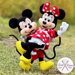 May include: Crocheted Mickey Mouse and Minnie Mouse dolls. Mickey is wearing yellow shoes and black shorts. Minnie is wearing a red dress with white polka dots, a red bow, and white gloves. The dolls are set against a blurred green background.