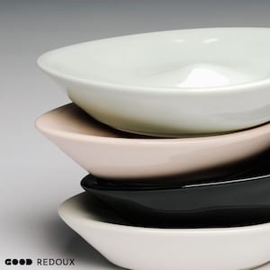 May include: A stack of four ceramic bowls in varying colors: white, beige, black, and off-white. The bowls have a smooth, glossy finish and a shallow, oval shape. The bowls are stacked on top of each other.