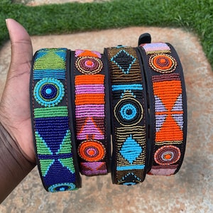 May include: Four beaded dog collars in a variety of colors. The collars are black leather with colorful beadwork in shades of blue, green, orange, pink, and brown. Each collar features a unique geometric design.