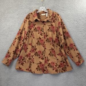 May include: Tan button-down shirt with a rose floral pattern in shades of pink and brown. The long-sleeved shirt has a collared neckline and is hanging on a clear hanger.