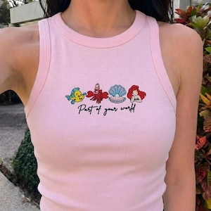May include: Pink tank top with embroidered cartoon characters and the text "Part of your world". The design features a yellow and blue fish, a red crab, a blue and white seashell, and a red-haired mermaid.