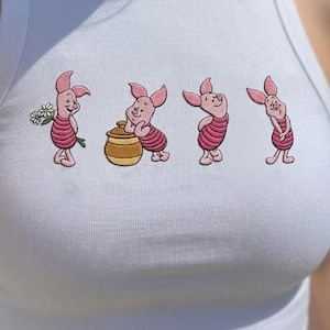 May include: White ribbed tank top featuring an embroidered design of four cartoon pigs in various poses. The pigs are pink with red striped clothing. One pig holds flowers, another leans on a honey pot.
