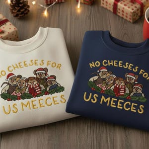 May include: Two crewneck sweatshirts, one cream and one navy blue, with embroidered text and a bear graphic. The text reads "NO CHEESES FOR US MEEECES". The bear graphic is wearing Santa hats and scarves.
