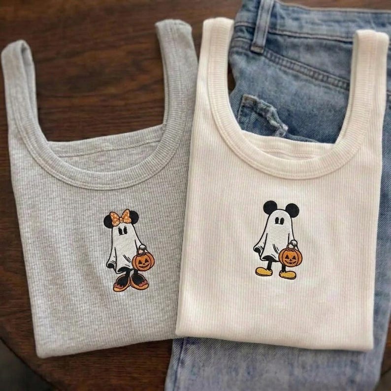May include: A grey ribbed tank top and a white ribbed tank top. The grey top features an embroidered ghost character with a bow and a pumpkin bucket. The white top features an embroidered ghost character with round ears and a pumpkin bucket.