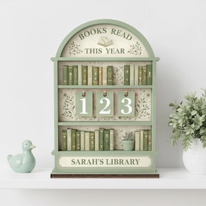 Puede incluir: Un estante en forma de librer&iacute;a verde salvia con el texto "BOOKS READ THIS YEAR" y "SARAH'S LIBRARY". Los estantes est&aacute;n llenos de libros en miniatura. El rastreador tiene tres etiquetas numeradas: 1, 2 y 3.
